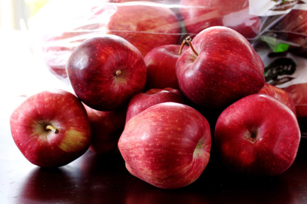 A pile of Red Delicious apples sitting on a dark wood table