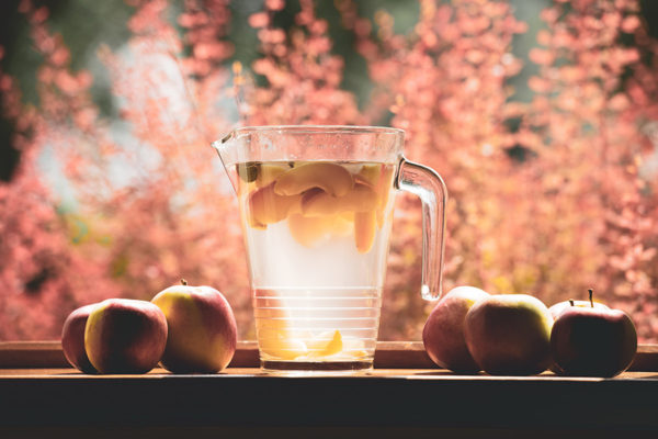 Apple drink in a pitcher with apples around it